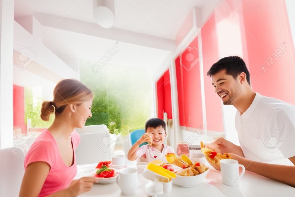glückliche junge Familie gesundes Frühstück in der Küche mit roten Details auf hellen Morgenlicht