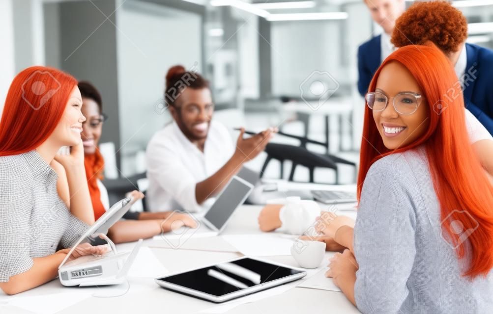 Redhead business woman with her multiethnic startup business team discussing new business plan, working on laptop and tablet computer while learning about drone technology for future business ventures