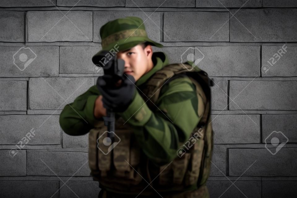 Un soldado en uniforme se para frente a un muro de piedra con equipo de guerra completo preparándose para la batalla