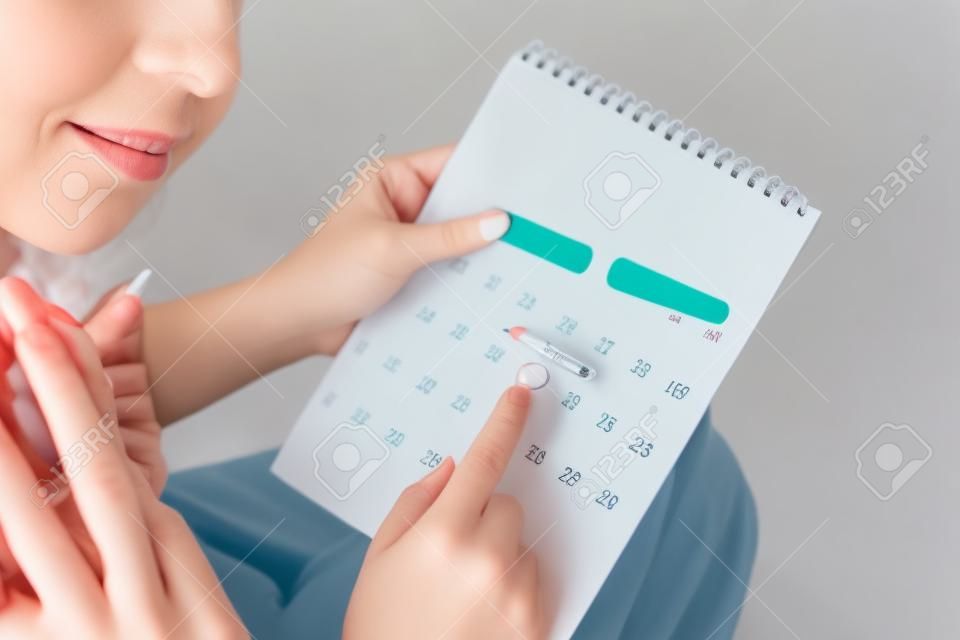 main de femme comptant la date sur le calendrier vérifiant son cycle menstruel planifiant le jour de l'ovulation une autre main tenant un test de grossesse