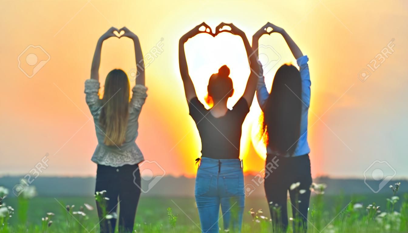 Five girls make a heart shape from their hands at sunset.