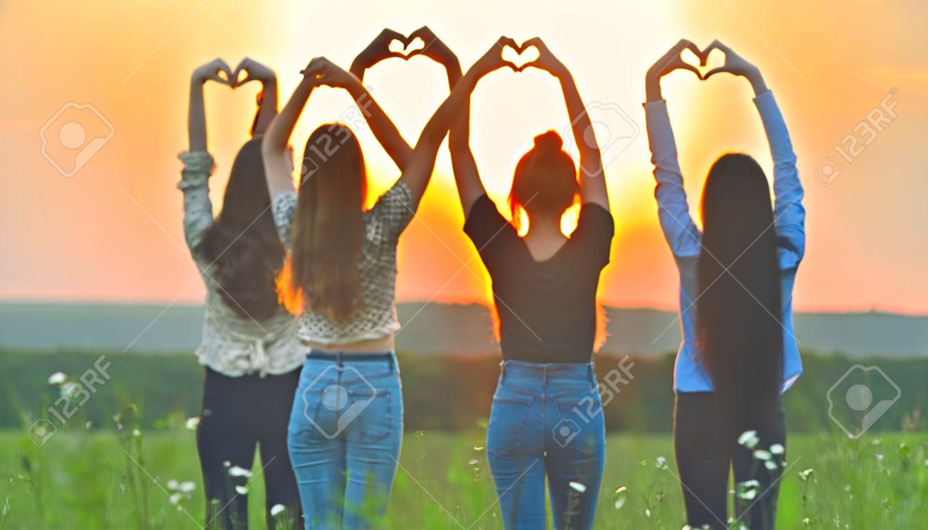 Fünf Mädchen formen bei Sonnenuntergang aus ihren Händen ein Herz.