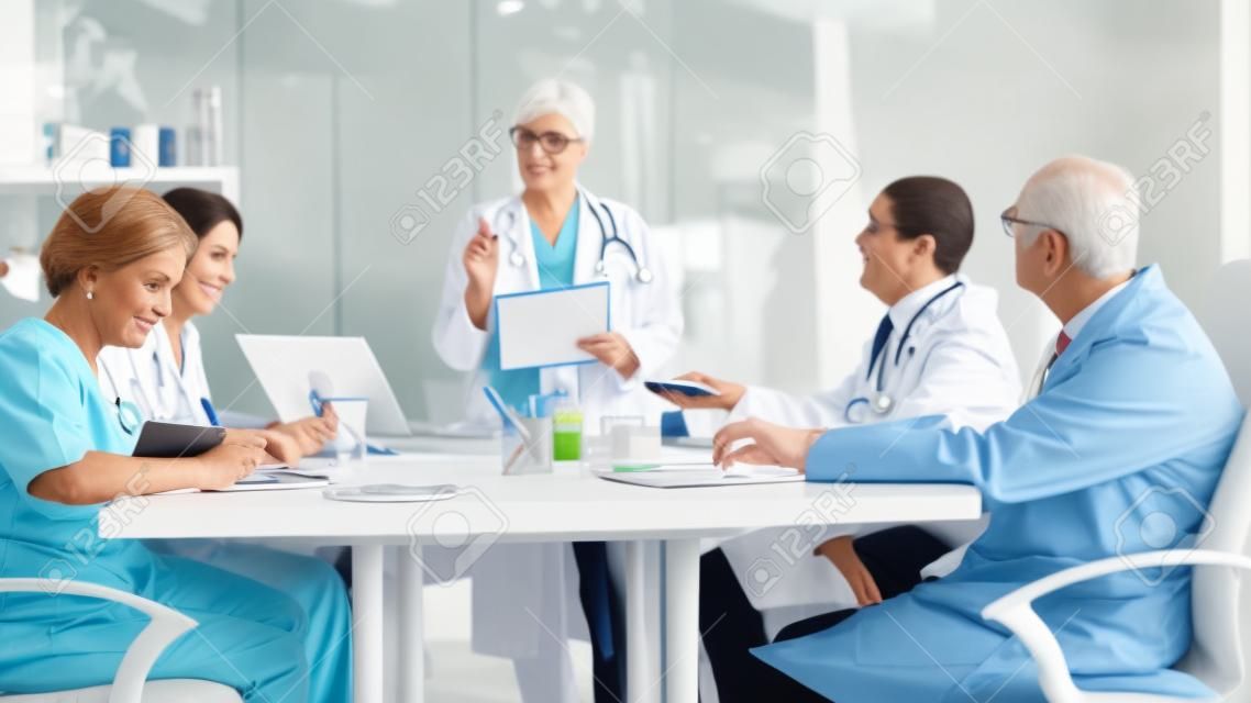 Porträt einer reifen Ärztin, die eine Ausschusssitzung beim Ärzterat leitet und neue medizinische Verfahren vorstellt, die am Schreibtisch stehen. Gruppe von Ärzten, die im Klinikbüro über Krankheitssymptome sprechen