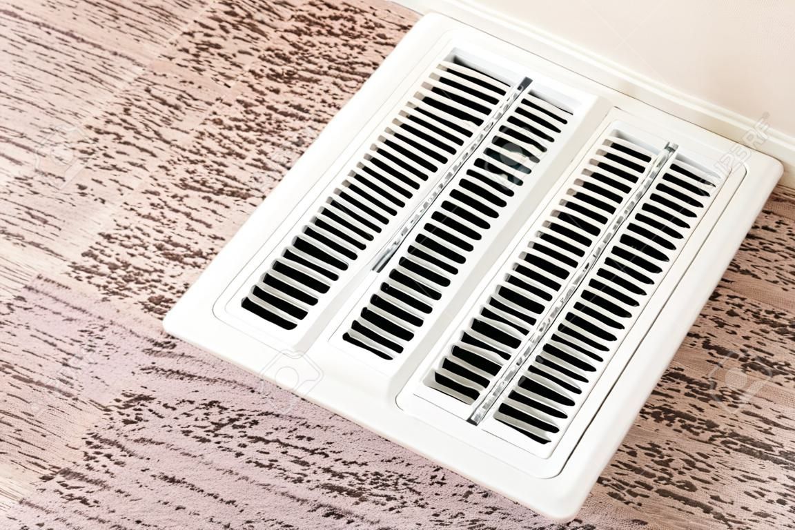 White air conditioner duct grille cover against floor with brown carpet. The cover has adjustable linear slots to direct air flow inside the room.