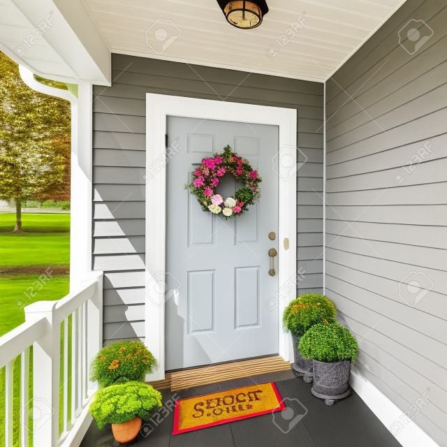 Square frame Front door porch with decorative displays of flower wreath and potted flowers at the floor