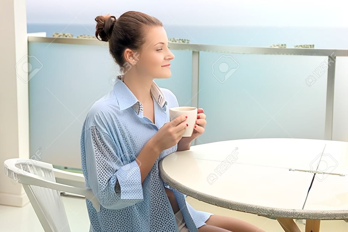 Mujer con camisa de hombre bebiendo café en la terraza de su casa