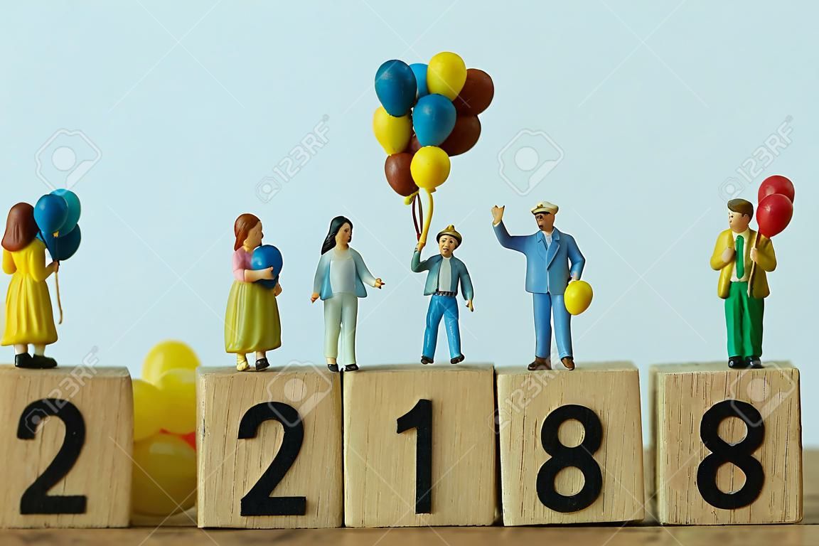miniature people happy family holding balloons standing on wooden block number 2018 with white background