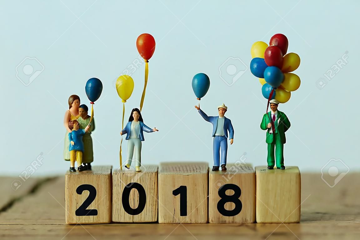miniature people happy family holding balloons standing on wooden block number 2018 with white background