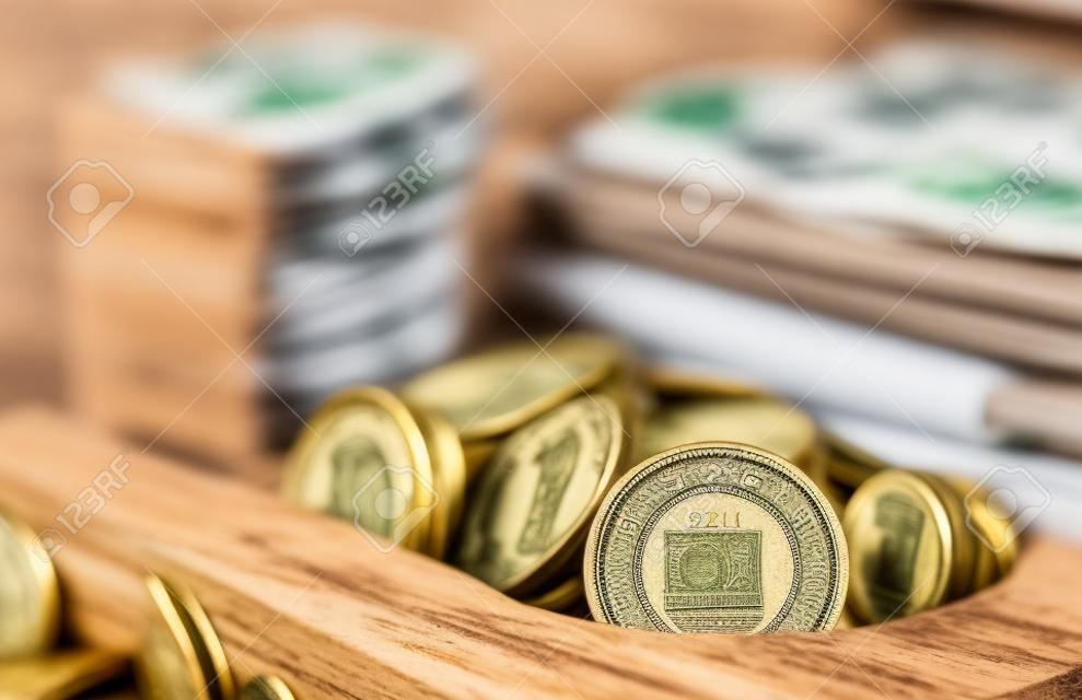 Vintage wooden box full of money: rolled up Polish zloty banknotes and coins from above on wooden surface. Concept of personal savings kept in cash at home and collecting for retirement