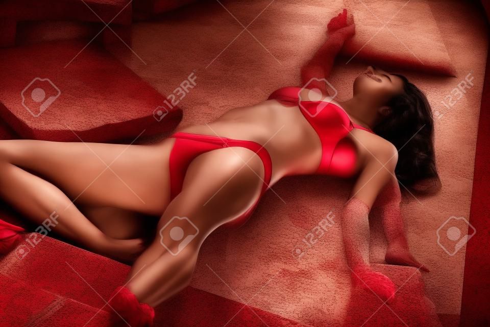 hermosa mujer jugando muerto, tirado en las escaleras en bikinis rojos