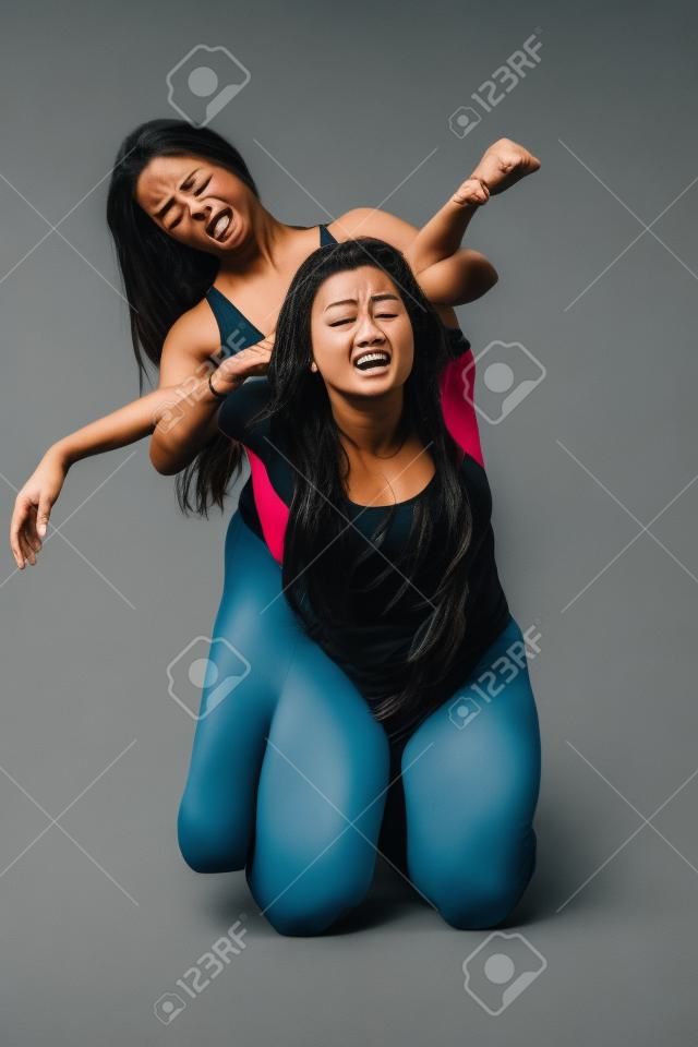 zwei Frauen auf dem Boden zu ringen über grauem Hintergrund