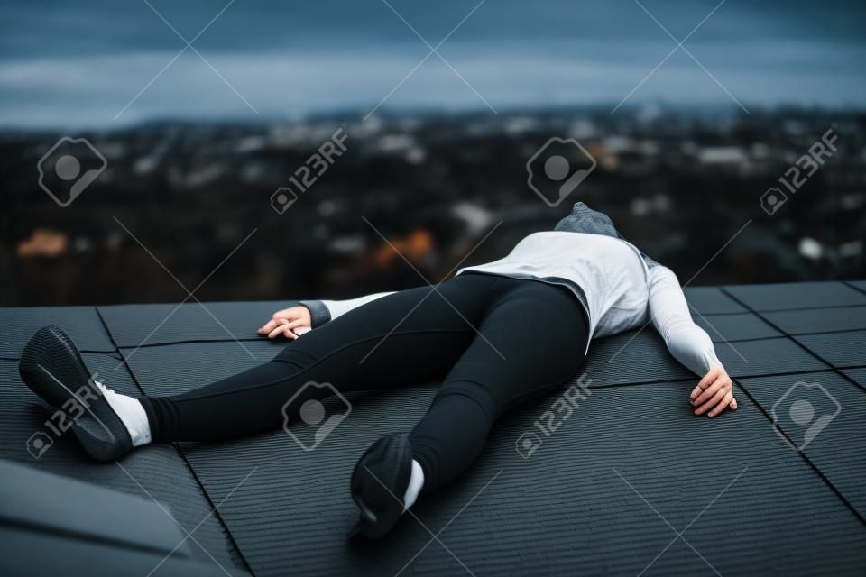犯罪シーン - 黒のレギンス不動は家の屋根の上に横たわる若い女性