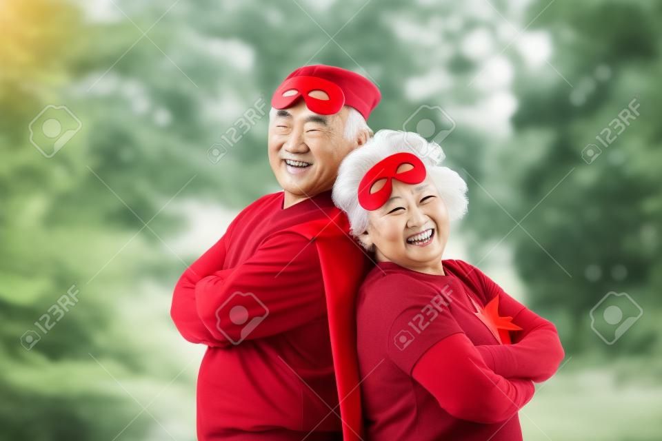 Una pareja mayor asiática disfrazada de superhéroe relajándose y sonriendo con los brazos cruzados en la unión al aire libre del parque. Copie el espacio. Mirando la cámara.