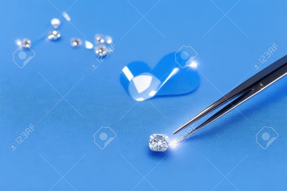 Cut diamond in hand close up with jewelry tools and scattering of different diamonds in background, front view on blue background. High quality photo