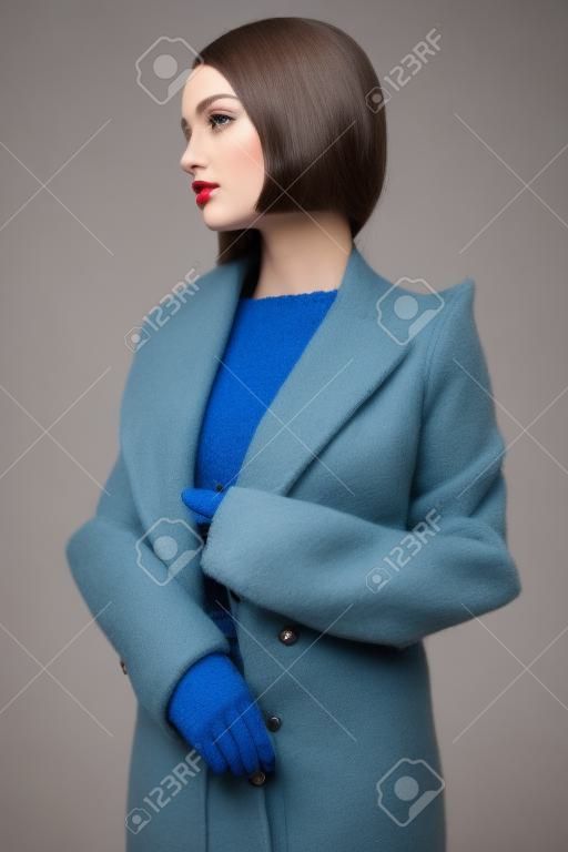 Beautiful sexy woman in blue autumn coat. Young pretty brunette pose in studio in vintage clothes. Fashionable lady with professional classic hairstyle. Fashion art portrait.