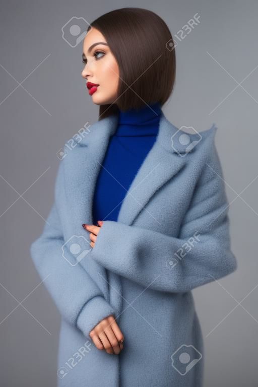 Bella donna in cappotto autunnale blu. Giovane bella posa castana in studio in abiti vintage. Signora alla moda con l'acconciatura classica professionale. Ritratto di arte di moda.