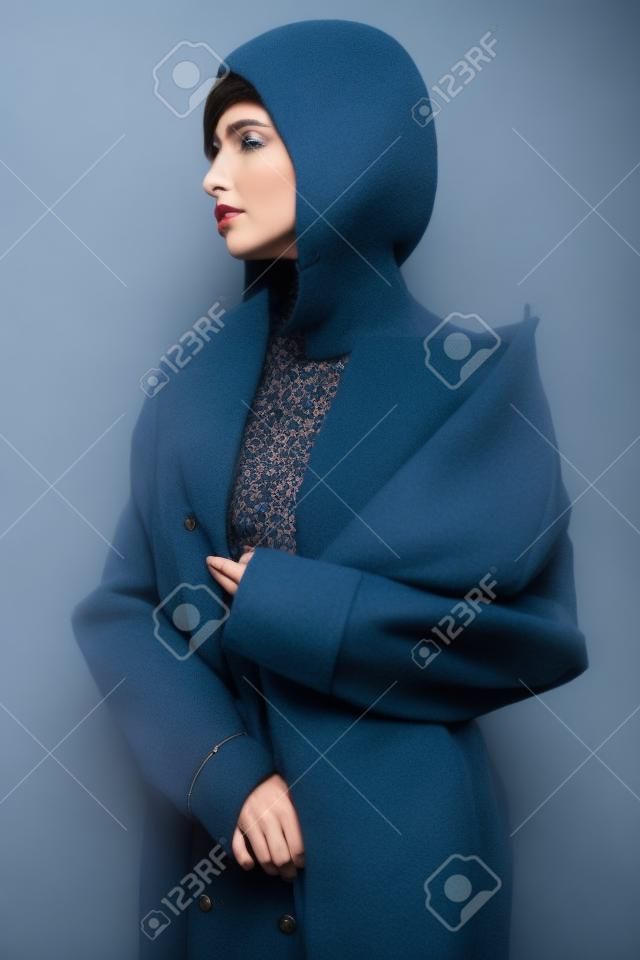 Mujer hermosa en abrigo azul de otoño. Pose bastante morena joven en estudio en ropa vintage. Dama de moda con peinado clásico profesional. Retrato de arte de moda.
