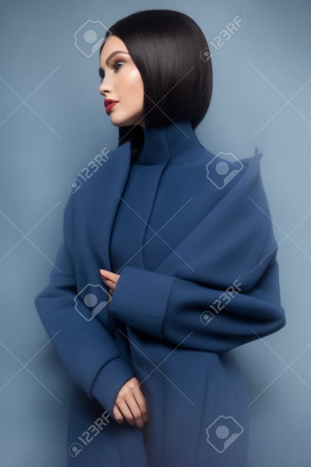 Beautiful sexy woman in blue autumn coat. Young pretty brunette pose in studio in vintage clothes. Fashionable lady with professional classic hairstyle. Fashion art portrait.