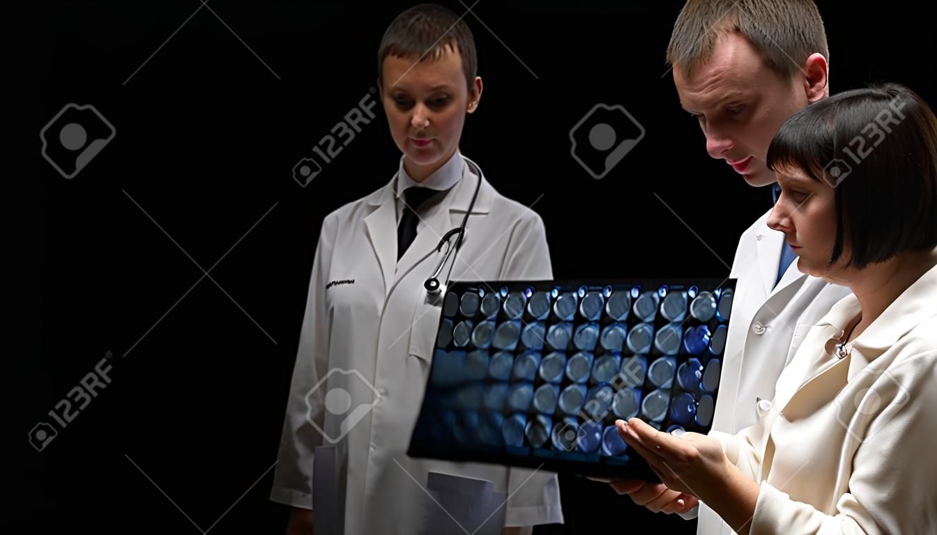 concetto Il paziente oncologico, la donna calva e l'uomo medico stanno visualizzando i risultati della tomografia su sfondo nero.