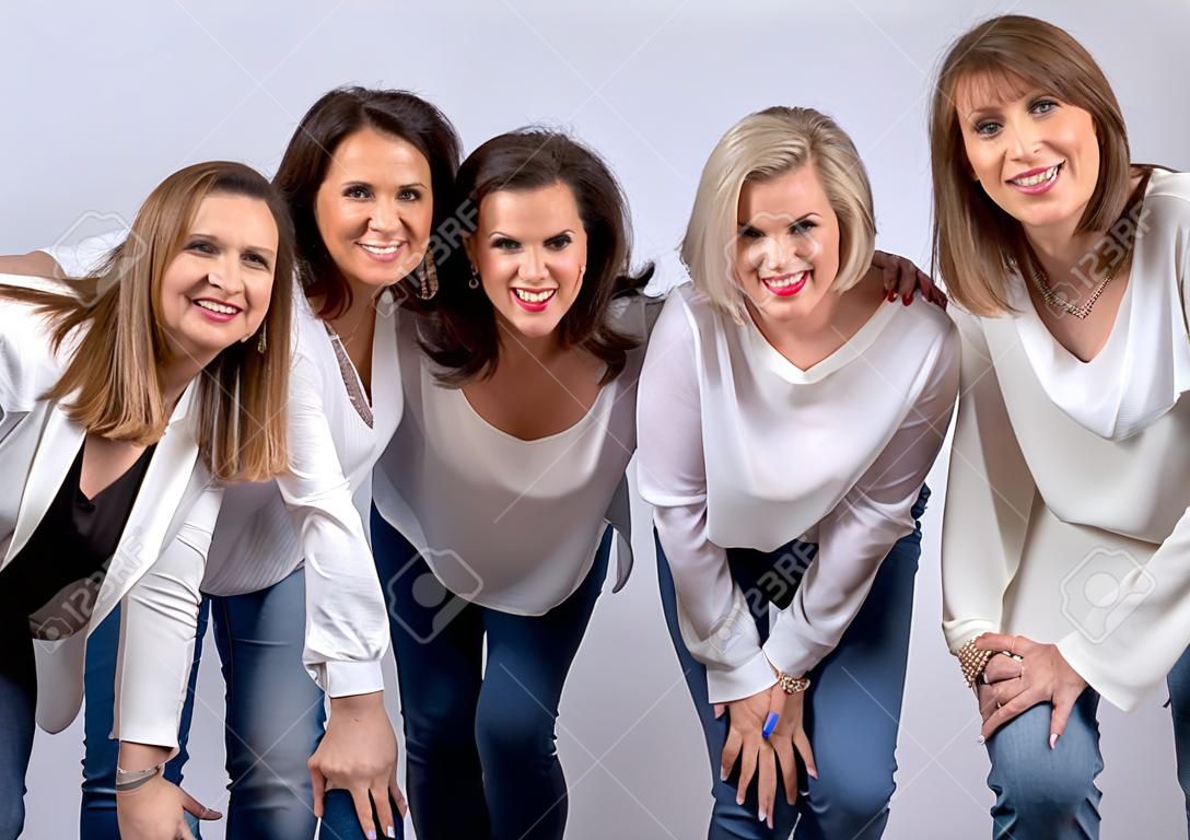 Group of 4 women, friends, middle-aged having fun in a photo session in a studio with white background