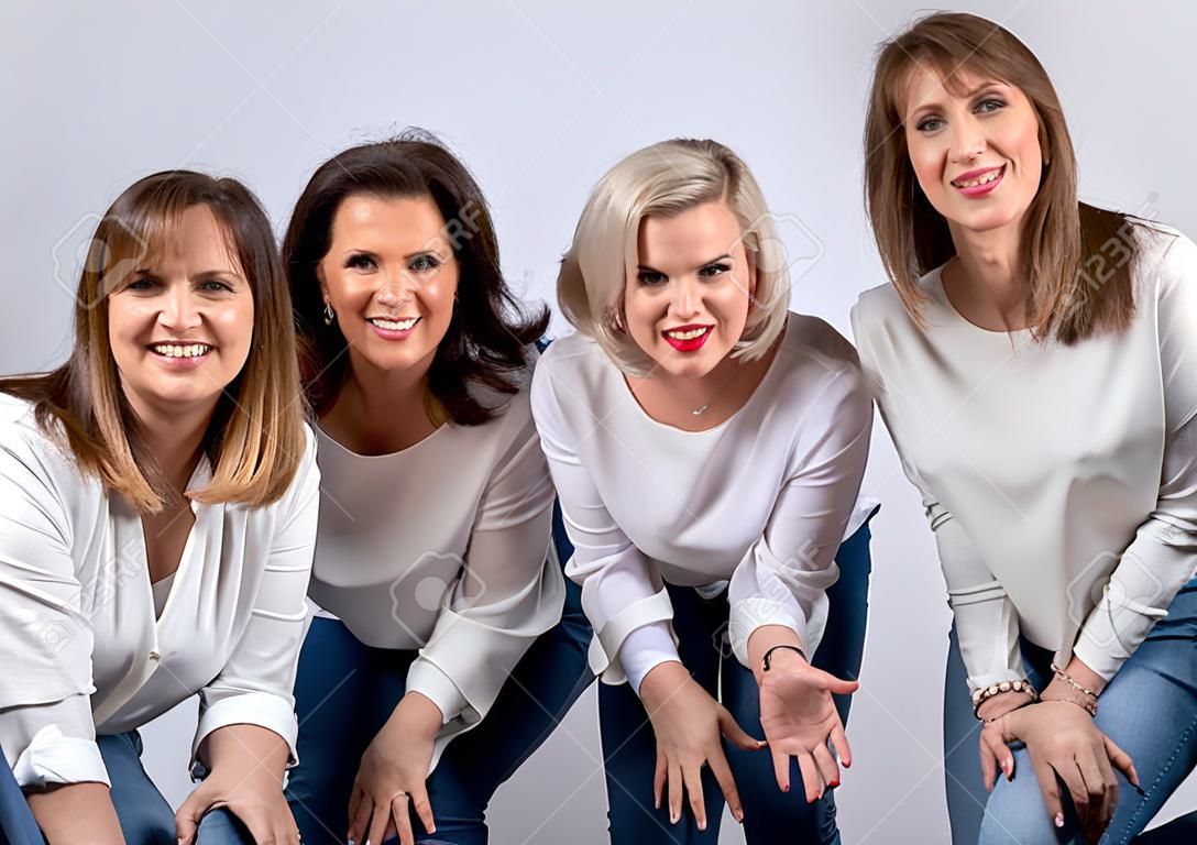 Group of 4 women, friends, middle-aged having fun in a photo session in a studio with white background