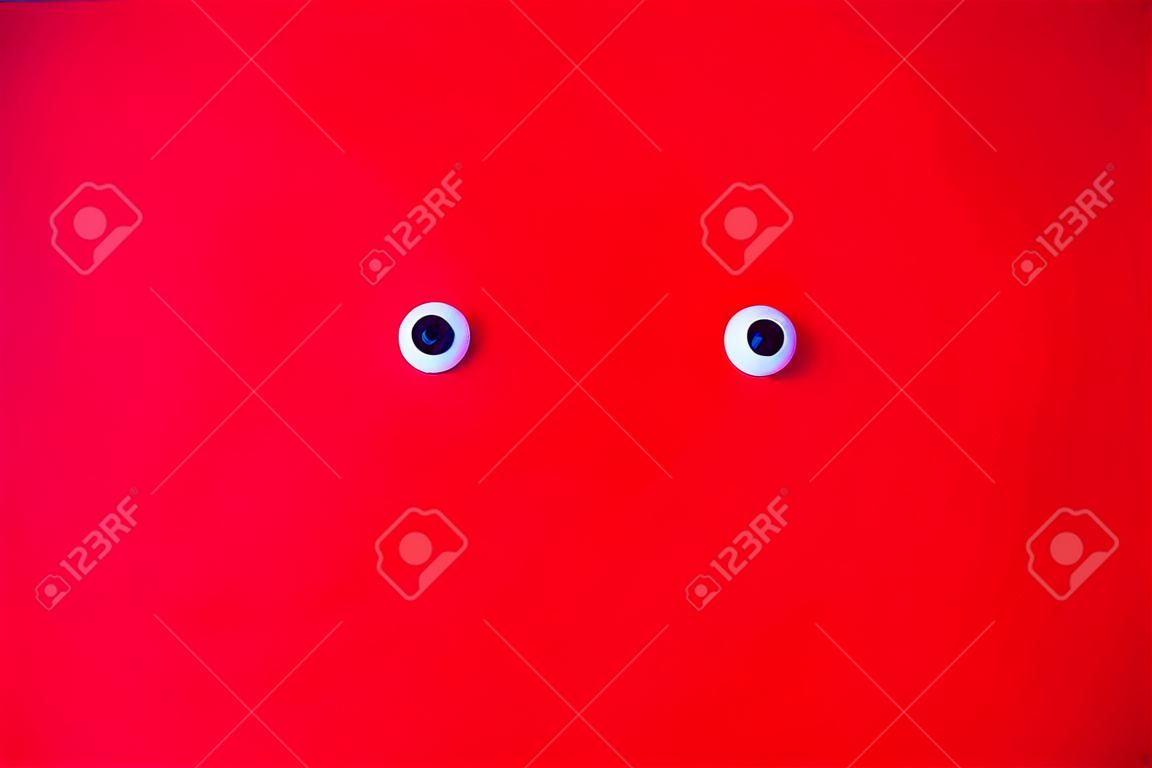 Roter Hintergrund mit den Augen des Spielzeugs kreative schwarze lustige Spielzeugaugen auf dem roten Hintergrund für Kunstillustration oder abstrakte Kreativität