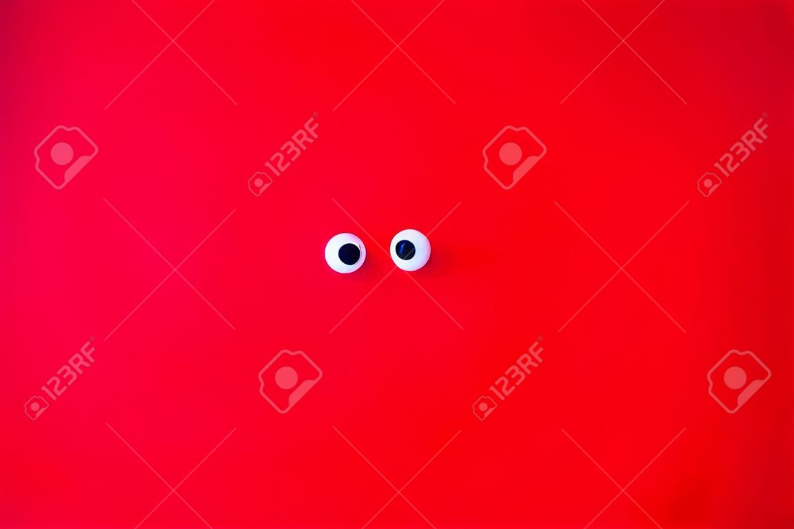 Roter Hintergrund mit den Augen des Spielzeugs kreative schwarze lustige Spielzeugaugen auf dem roten Hintergrund für Kunstillustration oder abstrakte Kreativität