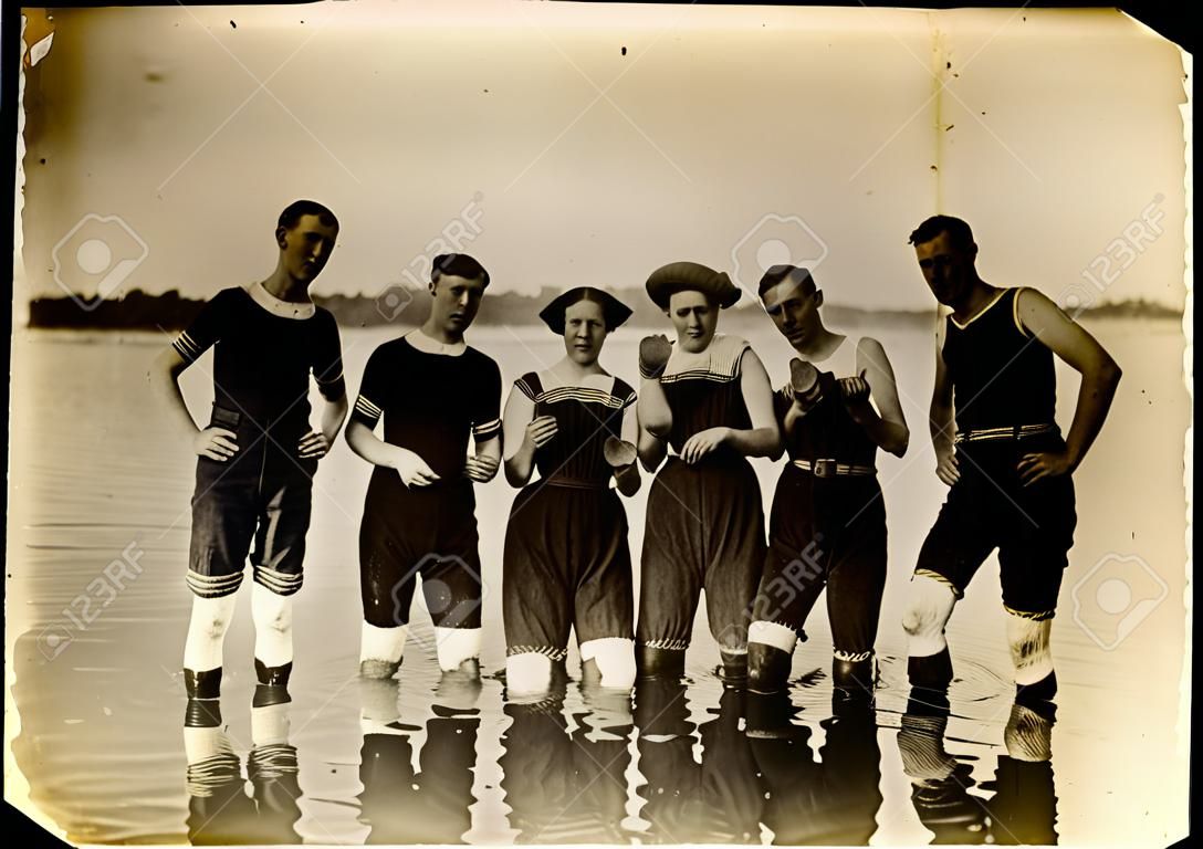 A szüreti úszók cipővel cipelnek a vízben. A Circa 1910 nyomtatás karcolással, műtárgyakkal, fakulással és szolarizálással rendelkezik.