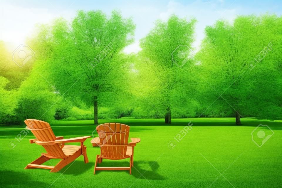 Two wooden adirondack chairs on lush green lawn with trees