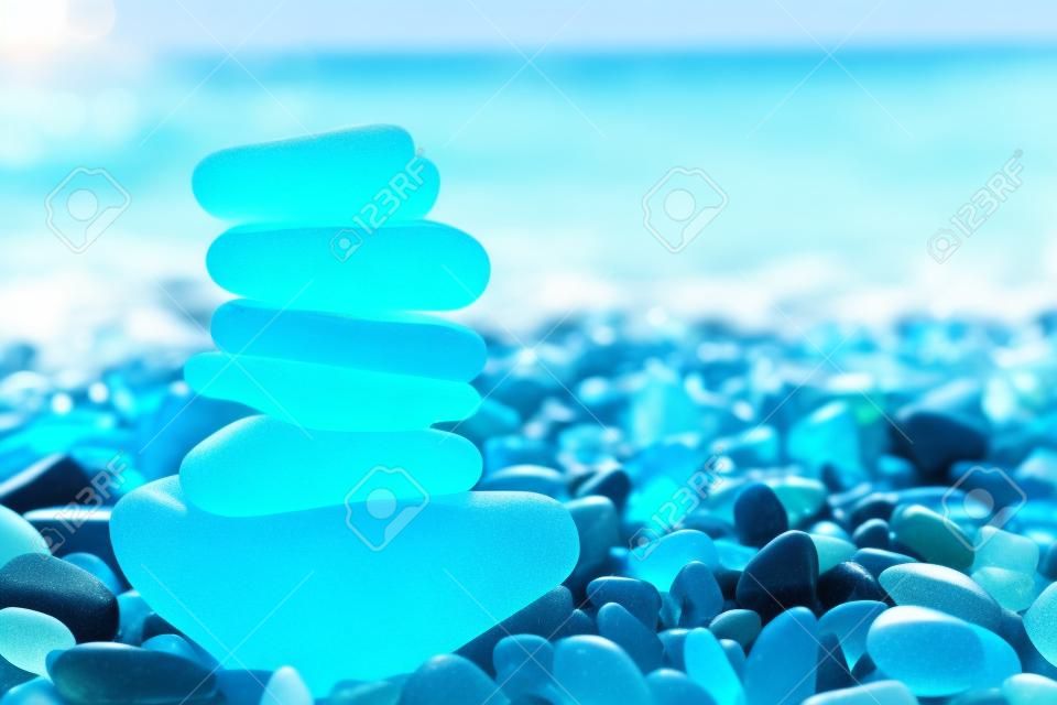 Kamienie ze szkła morskiego ułożone w piramidę równowagi na plaży. piękny lazurowy kolor morza z niewyraźnym tłem pejzażu morskiego. koncepcja medytacji i harmonii