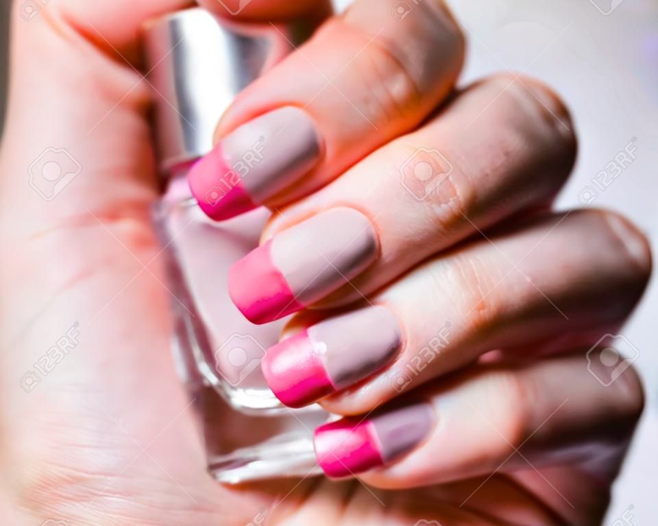 ネイルデザイン。灰色の背景に明るいピンクの春のマニキュアと手。女性の手のクローズアップ。アートネイル。
