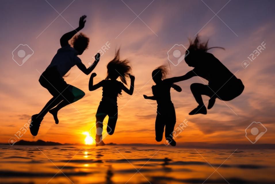 Силуэты счастливых молодых людей, прыжки в море на пляже на закате лета