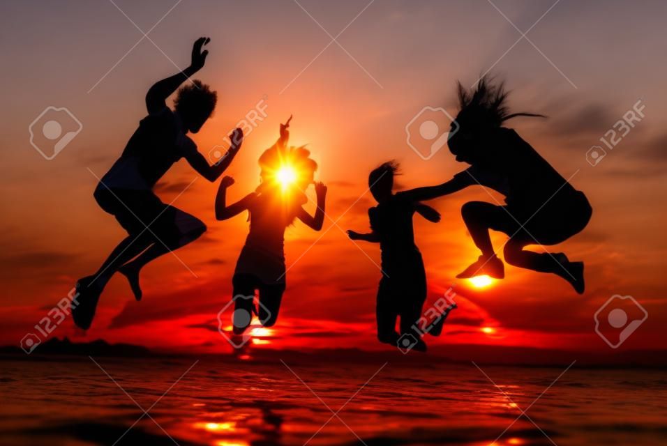 Silhouettes van gelukkige jonge mensen springen in zee op het strand op zomerzonsondergang