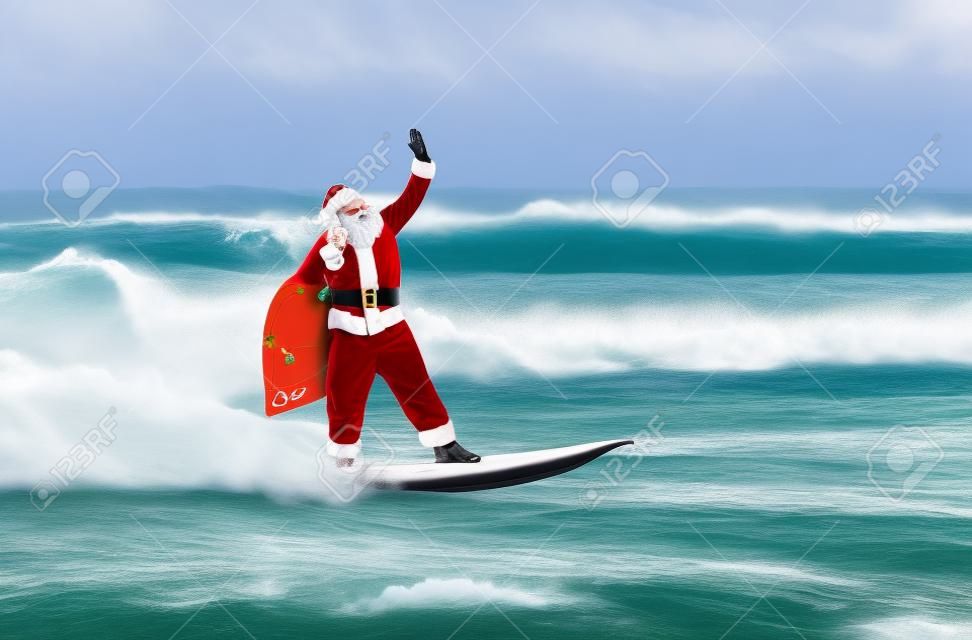 Weihnachtsmann mit großen Windsurfer Urlaub Geschenken Sack mit Surfbrett am Ozeanwellen surfen gehen spritzt bei windigem Wetter - Neujahr und Weihnachten aktiv Sport-Lifestyle-Konzept