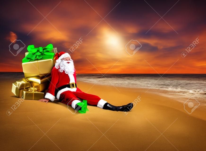 Natale Babbo Natale con il sacco pieno di scatole regalo d'oro con fiocchi rossi che riposano al mare spiaggia di sabbia tropicale - destinazioni di viaggio per le vacanze in paesi caldi concetto