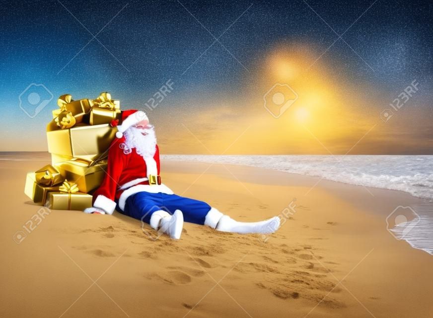 Natale Babbo Natale con il sacco pieno di scatole regalo d'oro con fiocchi rossi che riposano al mare spiaggia di sabbia tropicale - destinazioni di viaggio per le vacanze in paesi caldi concetto