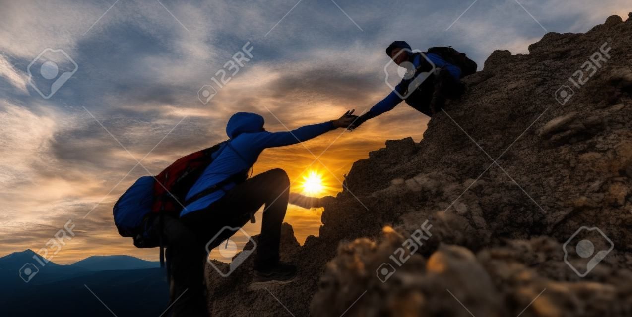 Coppia di escursionisti che si aiutano a vicenda a scalare una montagna al tramonto. Persone che danno una mano e un concetto di sport attivo.