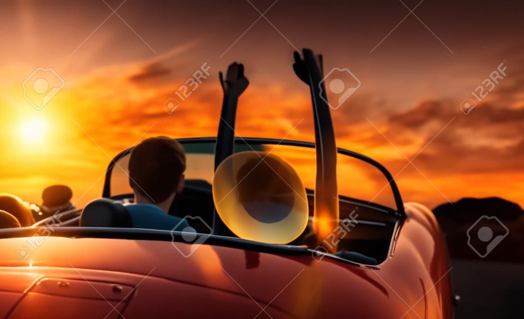 Fahren in den Sonnenuntergang. Glückliche junge Paar genießt den Sonnenuntergang in klassischer Weinlese-Sport-Auto-