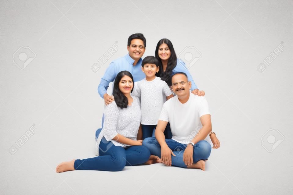 indian/asian family sitting over white background. senior and young couple with kids wearing white top and blue jeans. selective focus