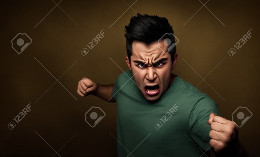 portrait of a angry young man. He is clenches fists and shouts.. The wicked guy beats .