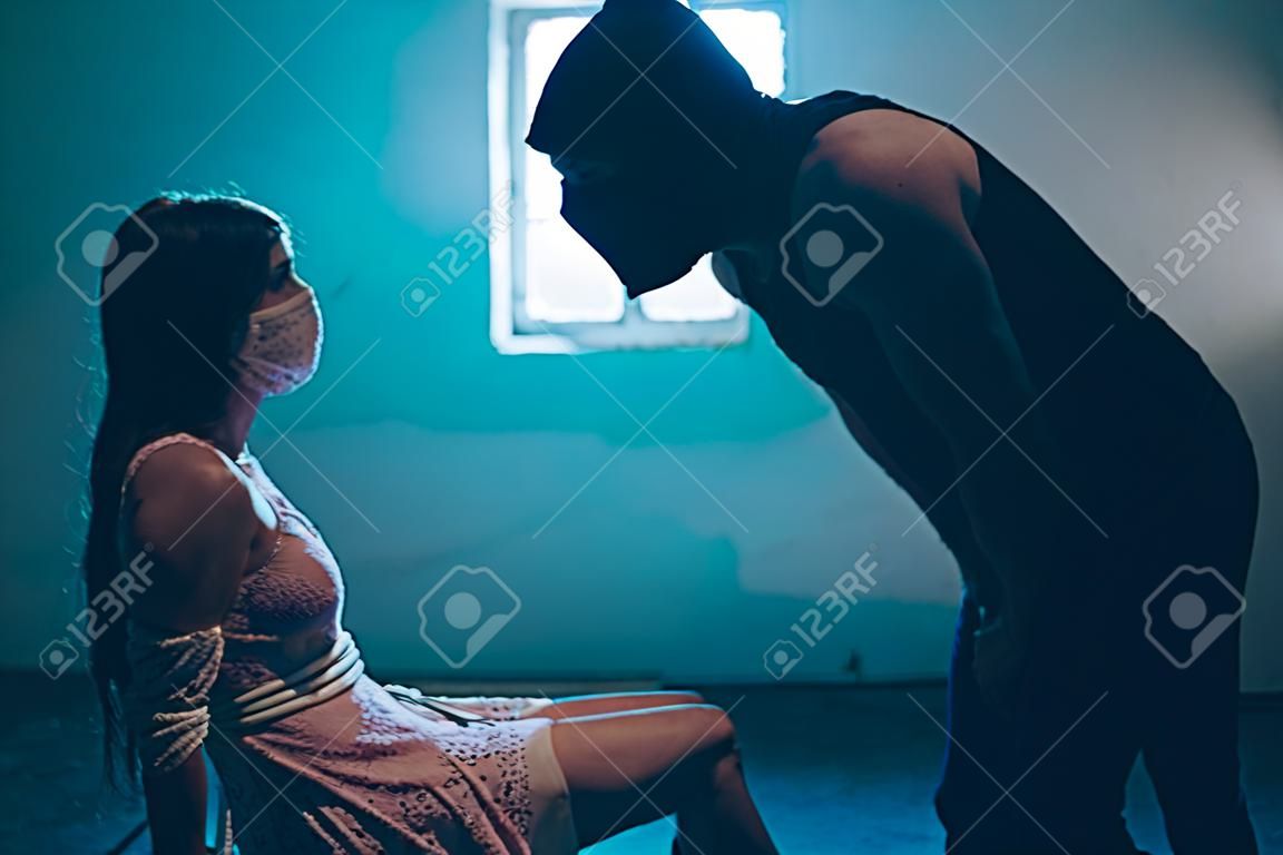 マスクを着た男は女の子の前に立って彼女を見ている。