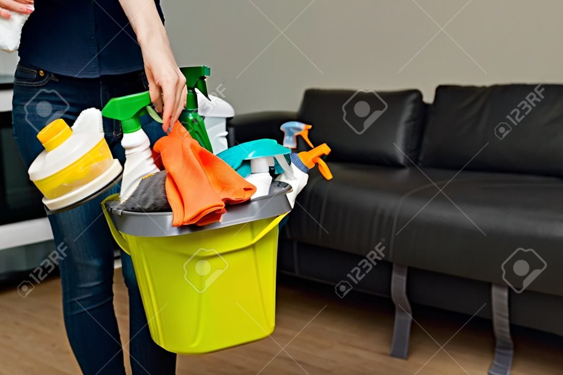 Kobieta trzyma detergenty w wiadrze na tle. kobieta jest gotowa do sprzątania domu. gospodyni sprząta dom.