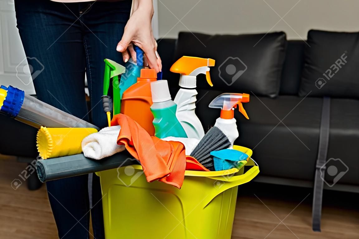 Una mujer sostiene detergentes en un balde en el fondo. La mujer está lista para limpiar la casa. Un ama de casa está limpiando la casa.