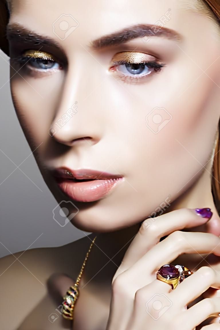 Gouden sieraden op mooie meisje. jonge blonde vrouw met make-up en juwelen accessoires.
