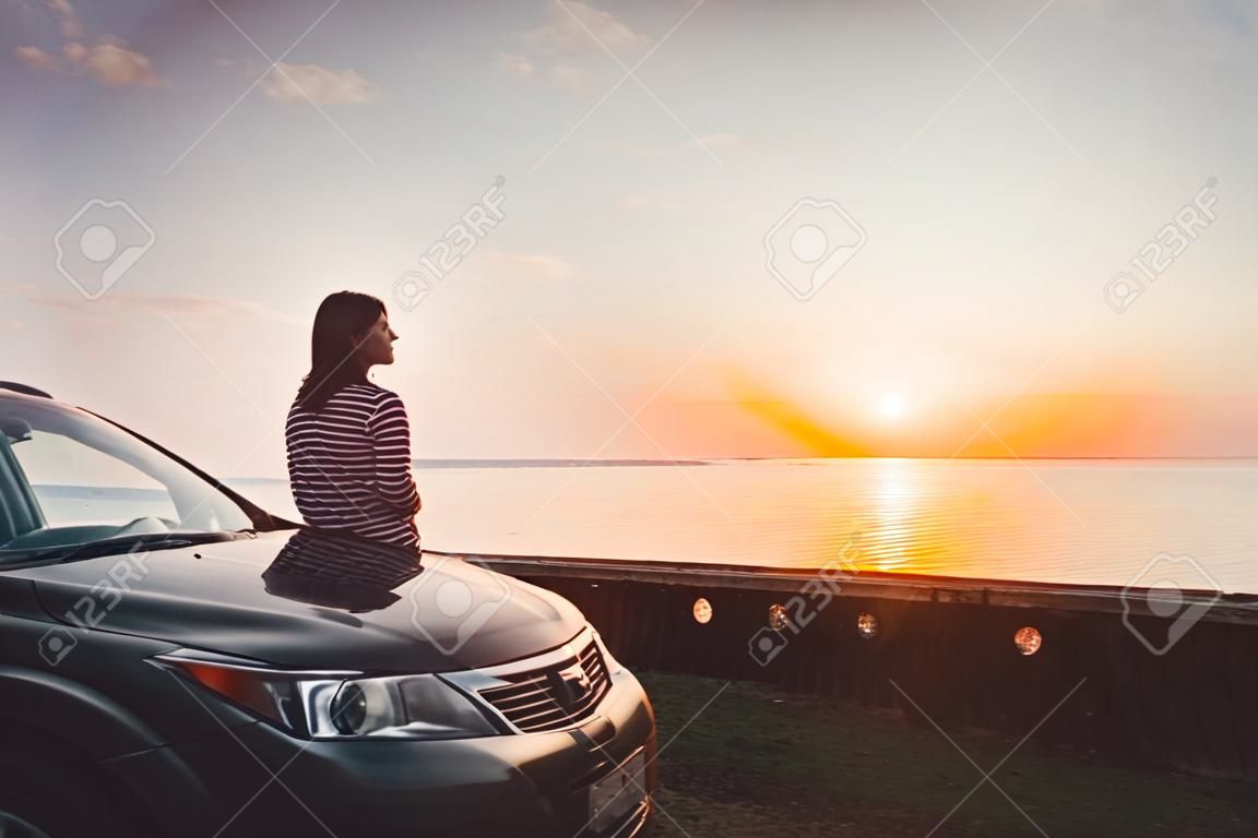 Biała brunetka stoi przy czarnym samochodzie i patrzy w prawo na romantycznym tle. Podróż i samotność. plaża, uciec. gruzińskie morze czarne.