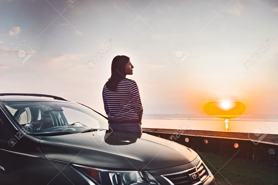 Biała brunetka stoi przy czarnym samochodzie i patrzy w prawo na romantycznym tle. Podróż i samotność. plaża, uciec. gruzińskie morze czarne.