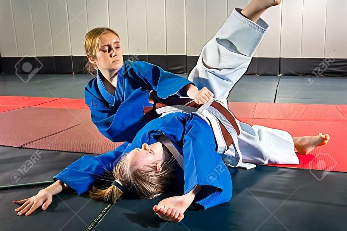 Uma jovem mulher em um quimono faz uma recepção dolorosa. Judô, jujitsu. Tatami, ginásio