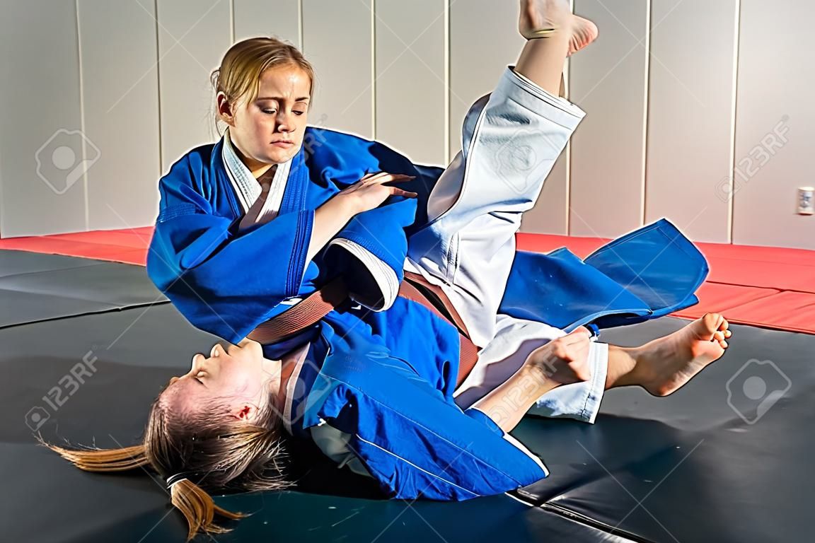 Uma jovem mulher em um quimono faz uma recepção dolorosa. Judô, jujitsu. Tatami, ginásio