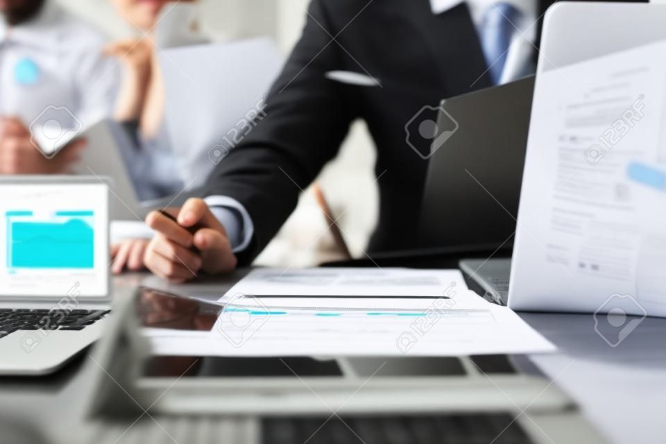 business documents on office table with smart phone and blank screen laptop computer and graph business diagram and two colleagues discussing data in the background,black and white