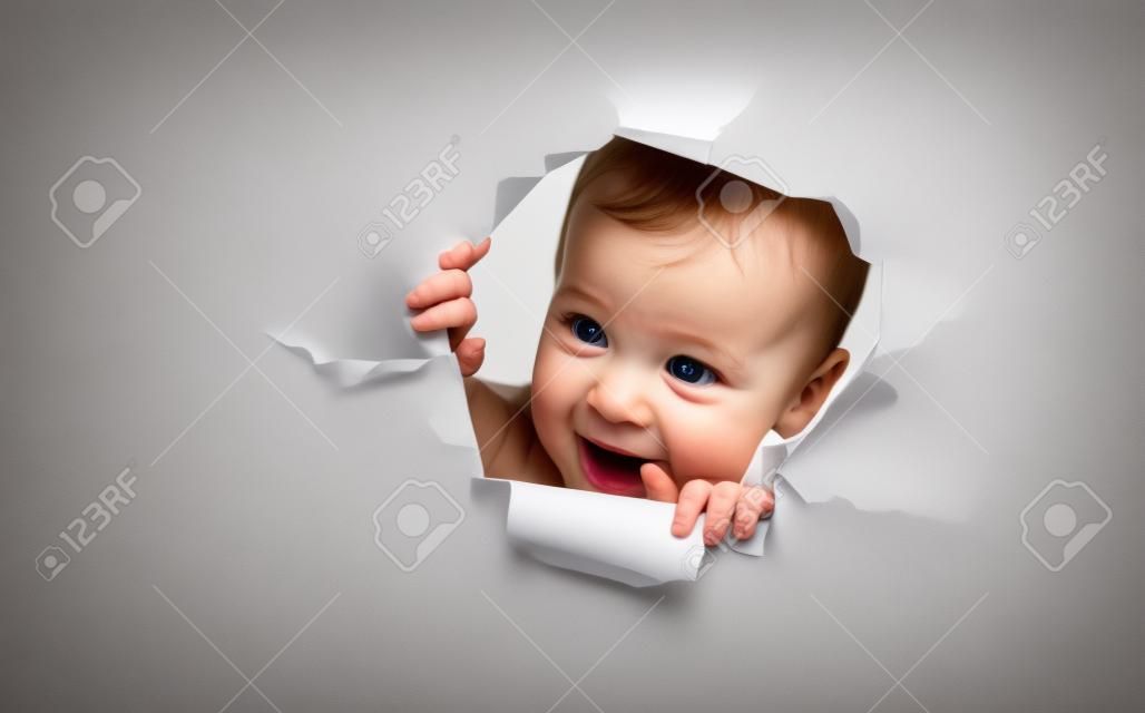 Забавный ребенок девочка выглядывает через отверстие в пустой белой бумаги плакат
